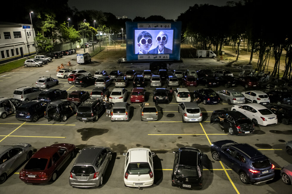 Dezenas de carros em um estacionamento virado para um telão onde está transmitindo um filme